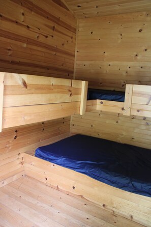 A wooden cabin interior with a bunk bed and a small enclosed sleeping area. - Ranch Cabin 22 (Portage)