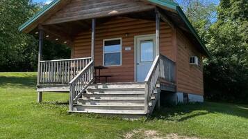 A wooden cabin with a porch, a front door, and a small window.