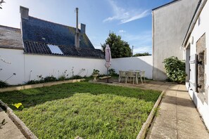A courtyard with a grassy area, a table with chairs, and a white wall with a blue-tiled roof.