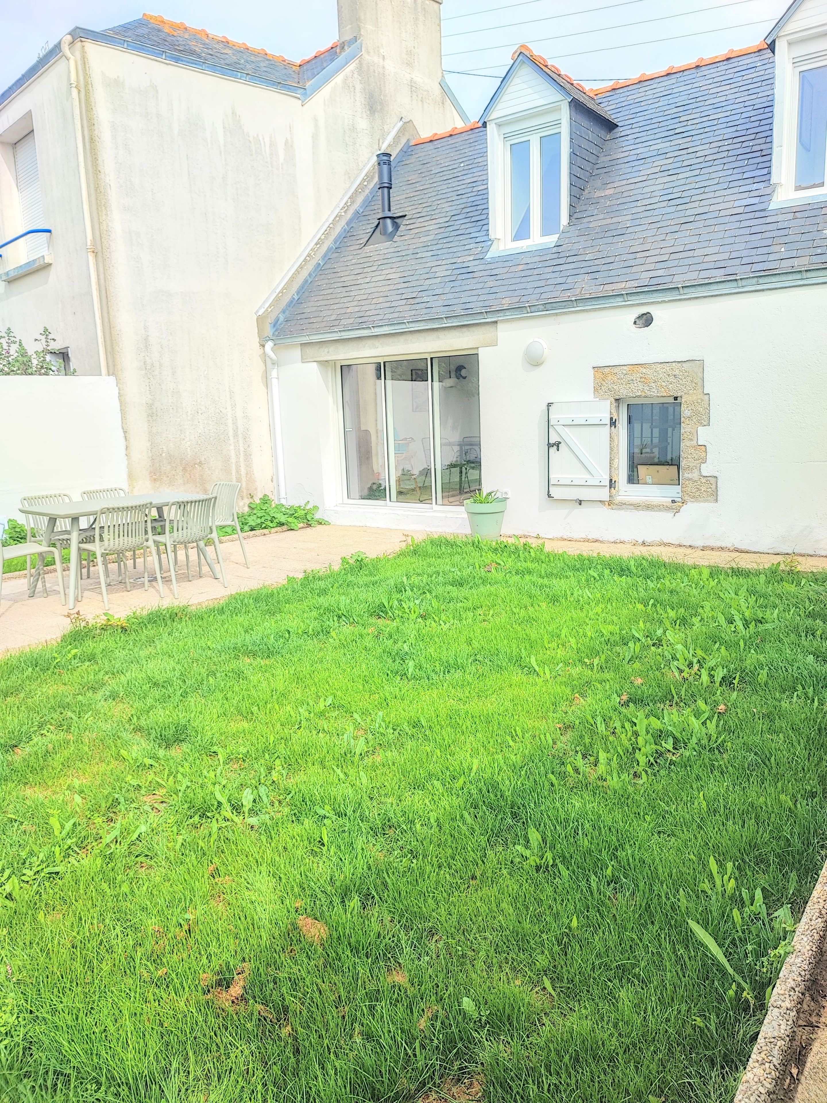 Une maison avec un toit en pente, une terrasse avec une table et des chaises, et une pelouse bien entretenue.