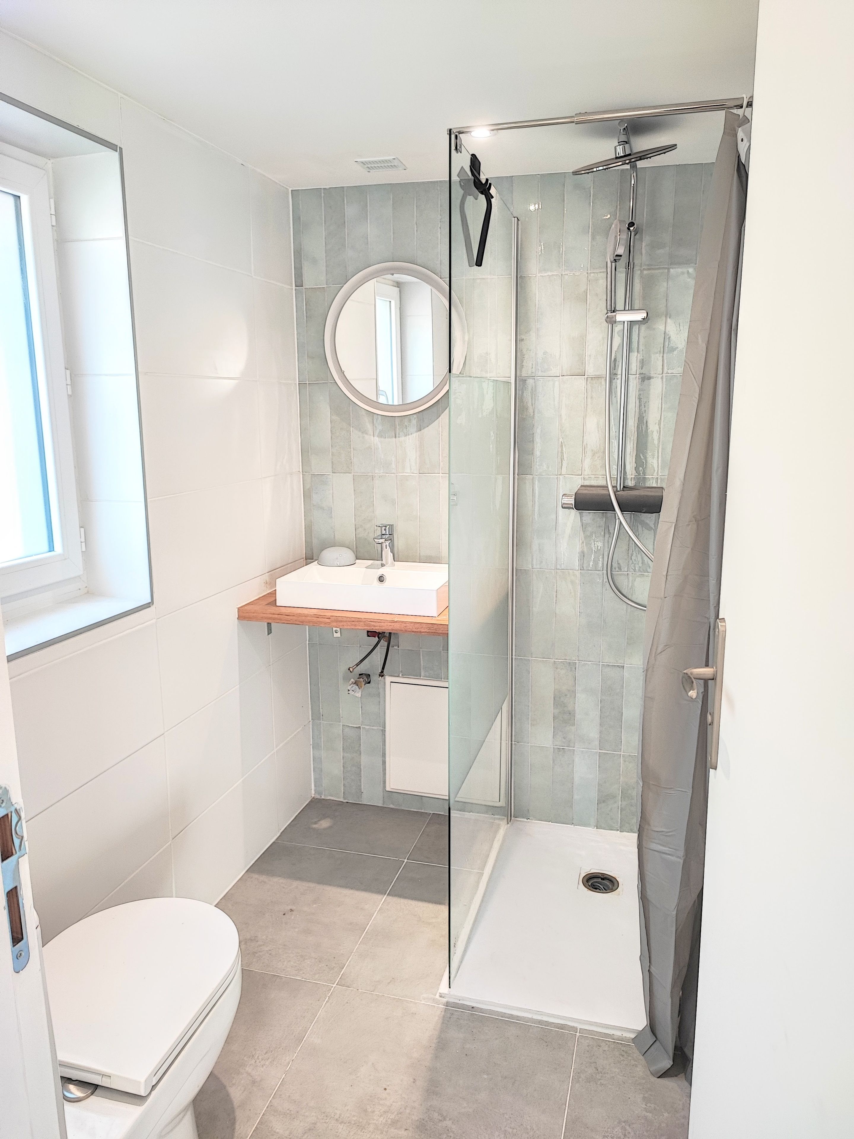 A modern bathroom with a glass-enclosed shower, a white toilet, and a sink with a mirror above it.