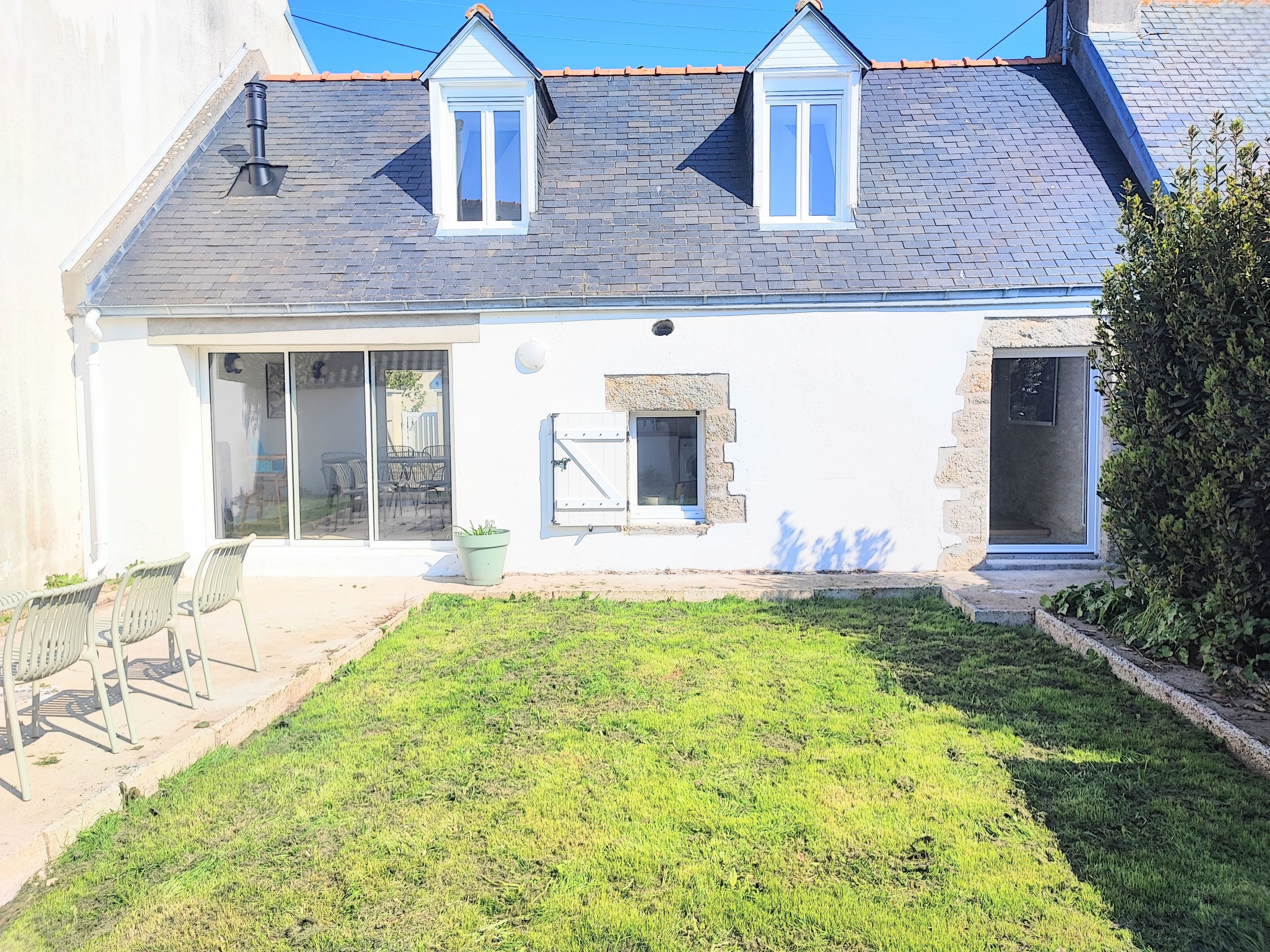 A two-story house with a sloped roof, a small garden, and a patio area with outdoor furniture.