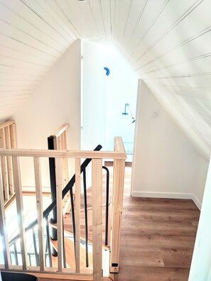 Un escalier en bois mène à une pièce lumineuse dotée d’une lucarne.