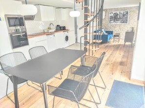 Une cuisine moderne dotée d’appareils électroménagers intégrés, un coin repas avec des chaises en métal et un escalier menant à une mezzanine.