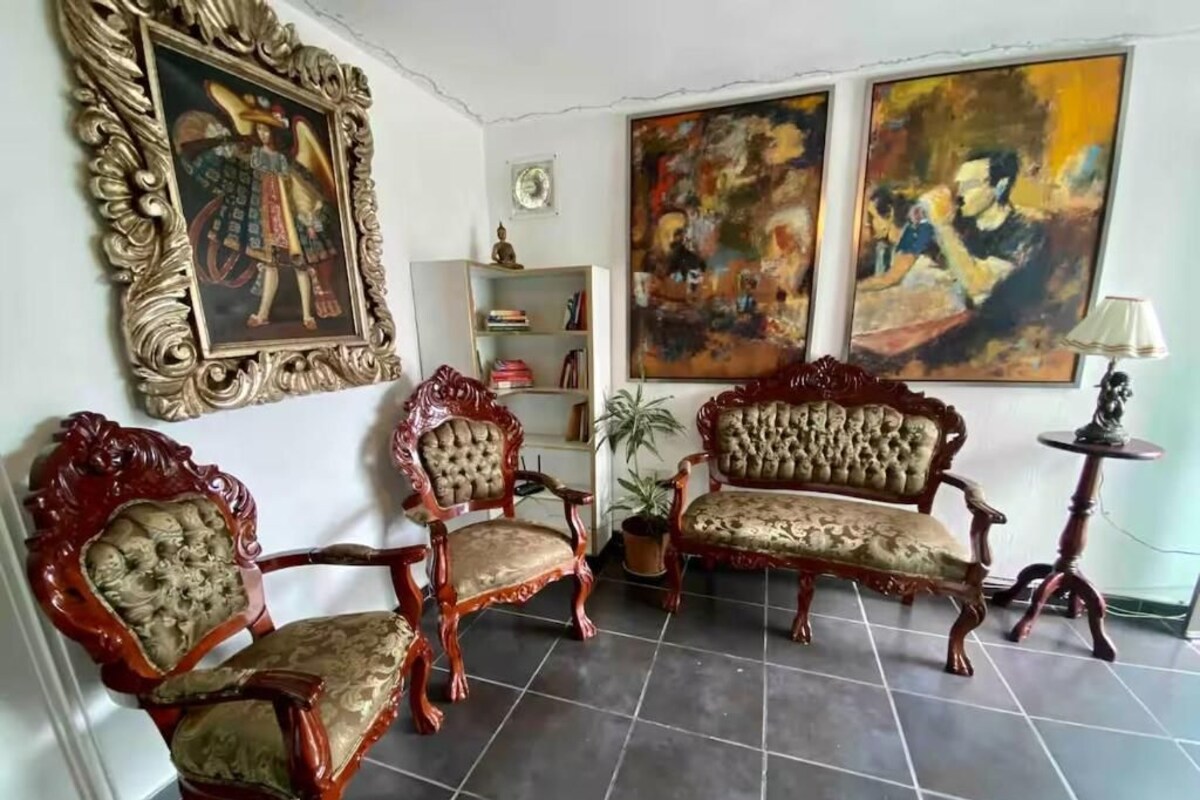 A room with a sofa, two chairs, a small table, and a potted plant.
