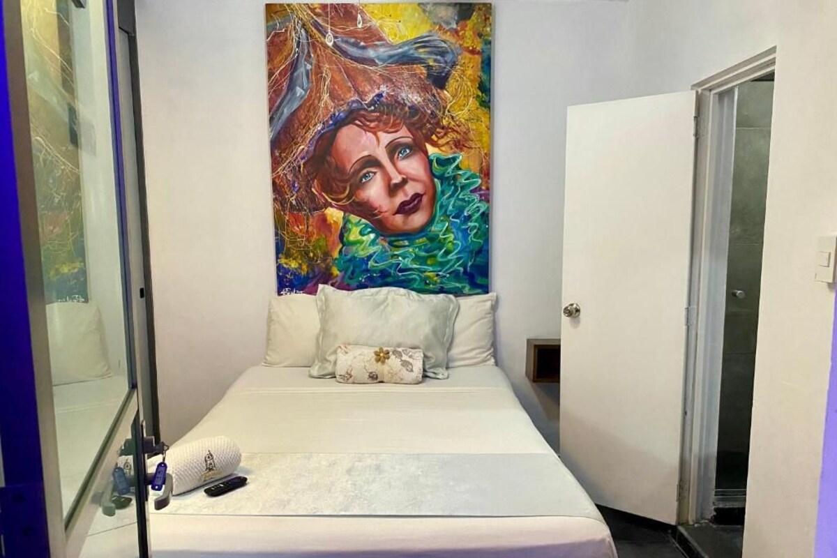 A hotel room with a bed, a painting on the wall, and a door.