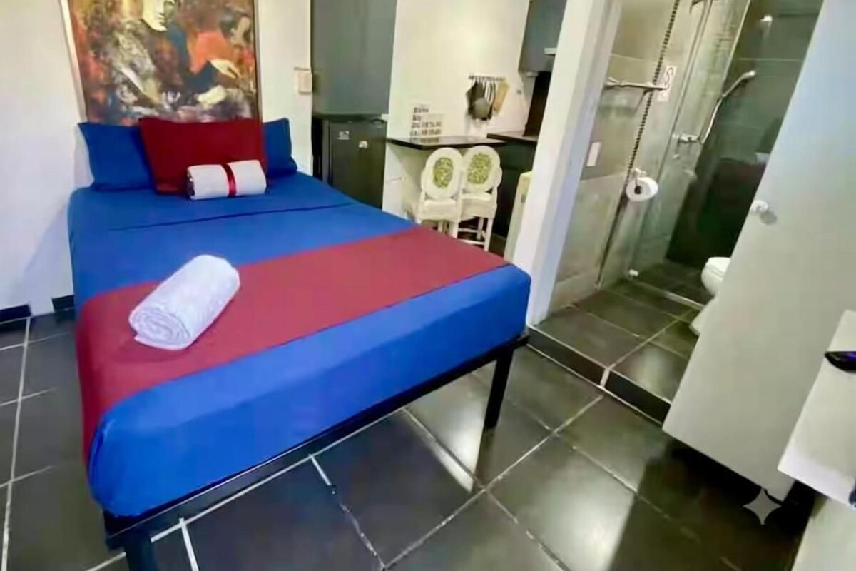 A hotel room with a bed, a painting on the wall, and a bathroom visible through an open door.