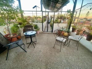 A covered outdoor seating area with a table and chairs, surrounded by potted plants and a metal gate leading to a staircase. - Suites Casa Pajaritos (Guadalajara)