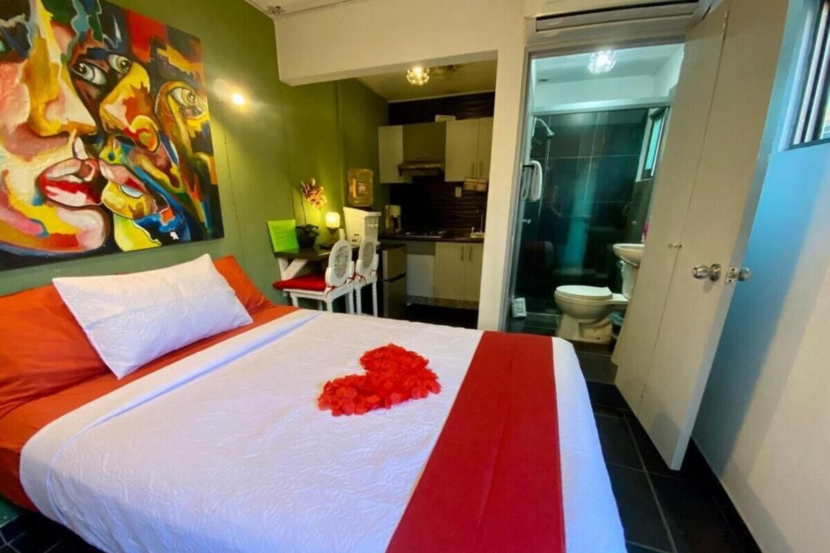 A hotel room with a bed, a painting on the wall, and a view into the bathroom.