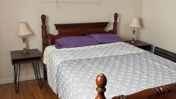 Ein Schlafzimmer mit einem hölzernen Bett, zwei Nachttischen mit Lampen, einem Fenster mit Jalousien und einem Sessel.