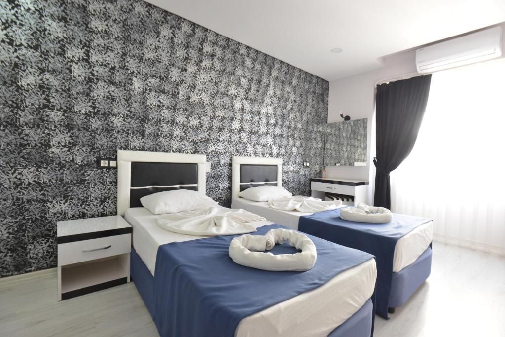 A hotel room with two beds, a nightstand, a desk, and a window with curtains.