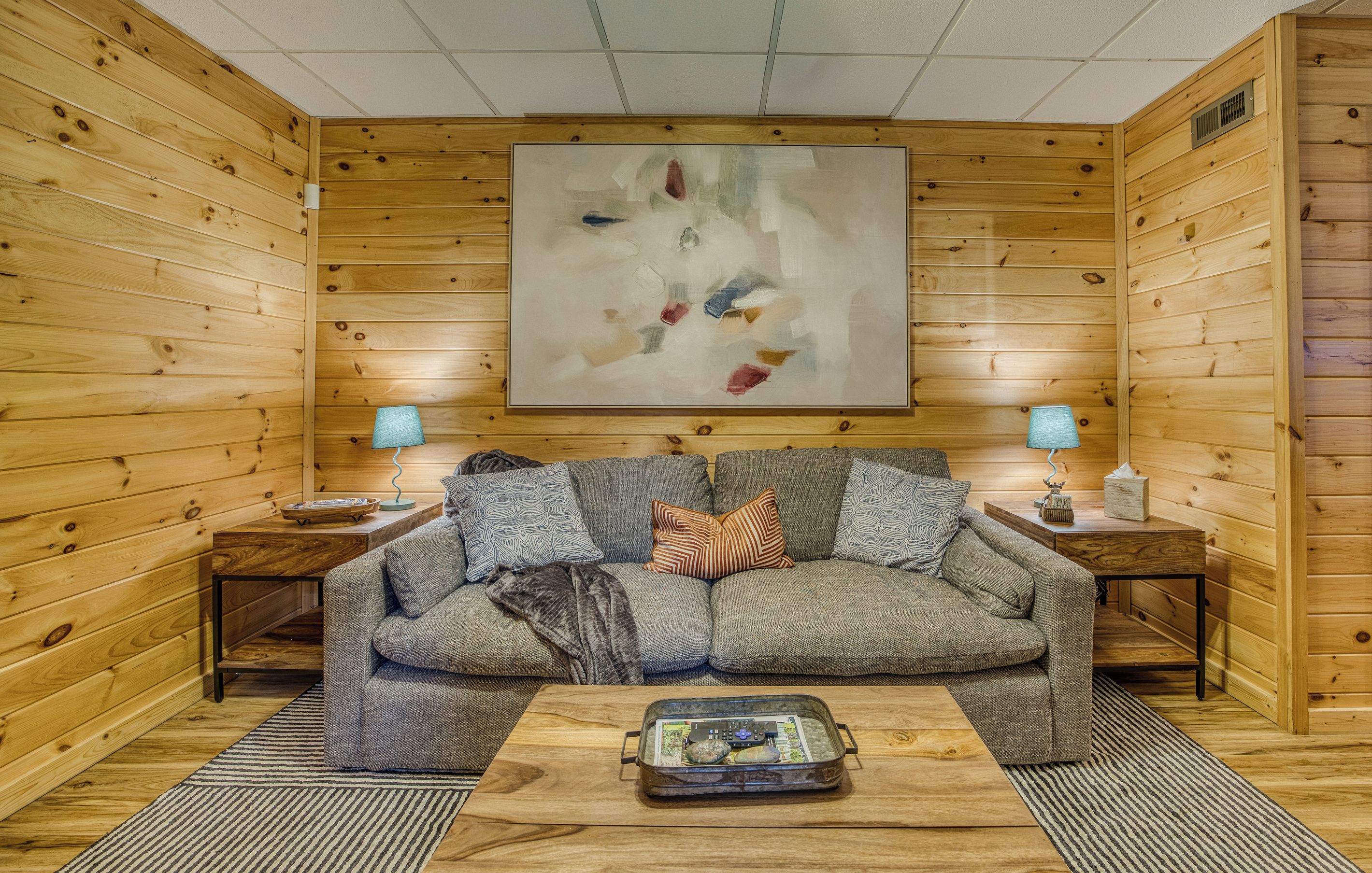 A cozy room with a wooden interior, a sofa, two lamps, and a painting on the wall.