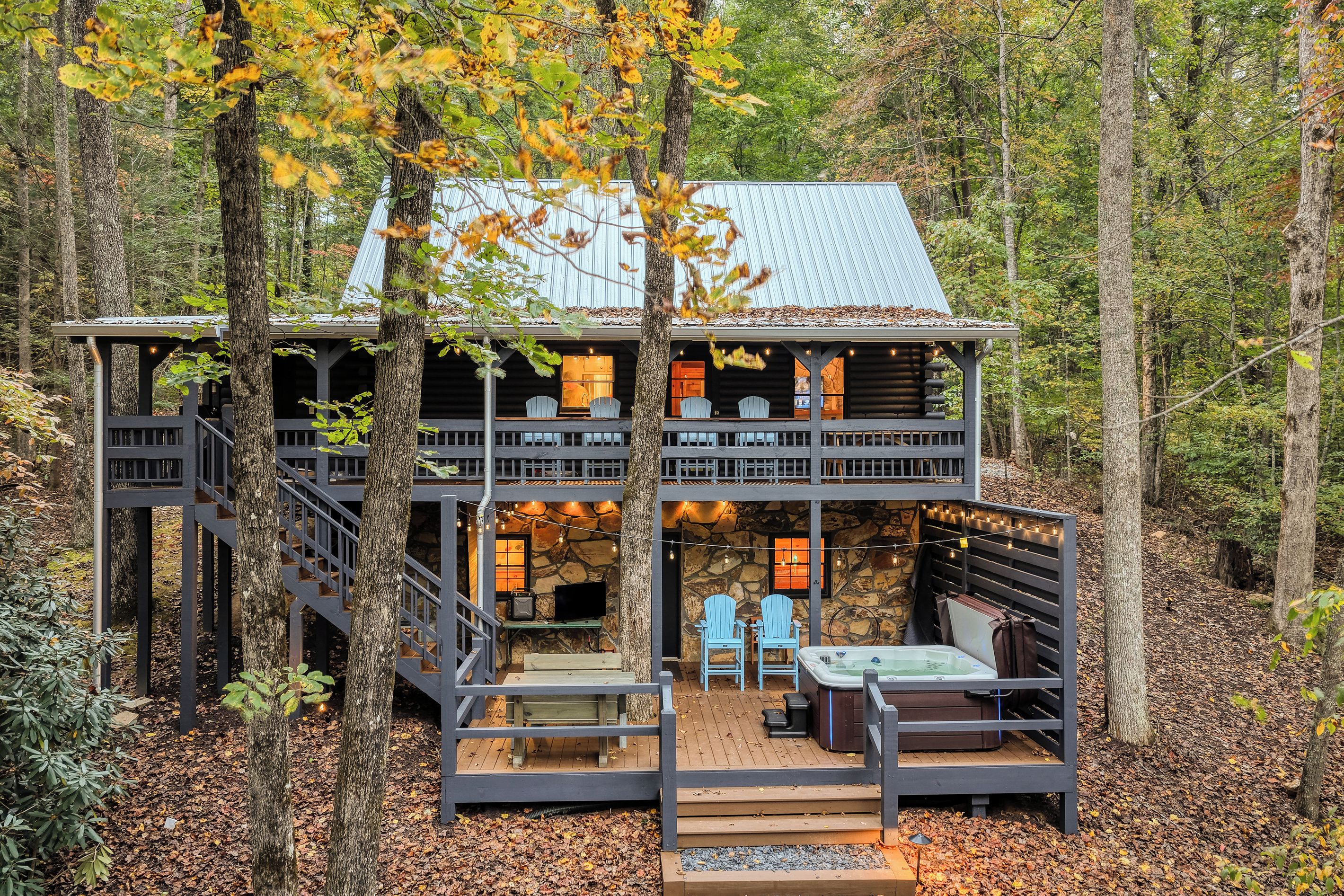 A cabin with a stone exterior, two decks, outdoor seating, and a hot tub.
