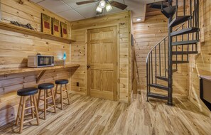 A wooden interior with a kitchen area, a microwave, stools, and a spiral staircase. - Laurel Lodge on Fightingtown Creek (Blue Ridge,)