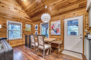 Interno di una baita in legno con zona pranzo, sedie, tavolo e opere d'arte alle pareti.