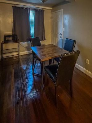 Un comedor con una mesa y sillas de madera, un microondas sobre una mesita y una puerta con interruptor de luz.