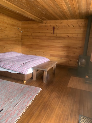 Ein Interieur einer Holzhütte mit einem Bett, einer Bank und einem Holzofen.