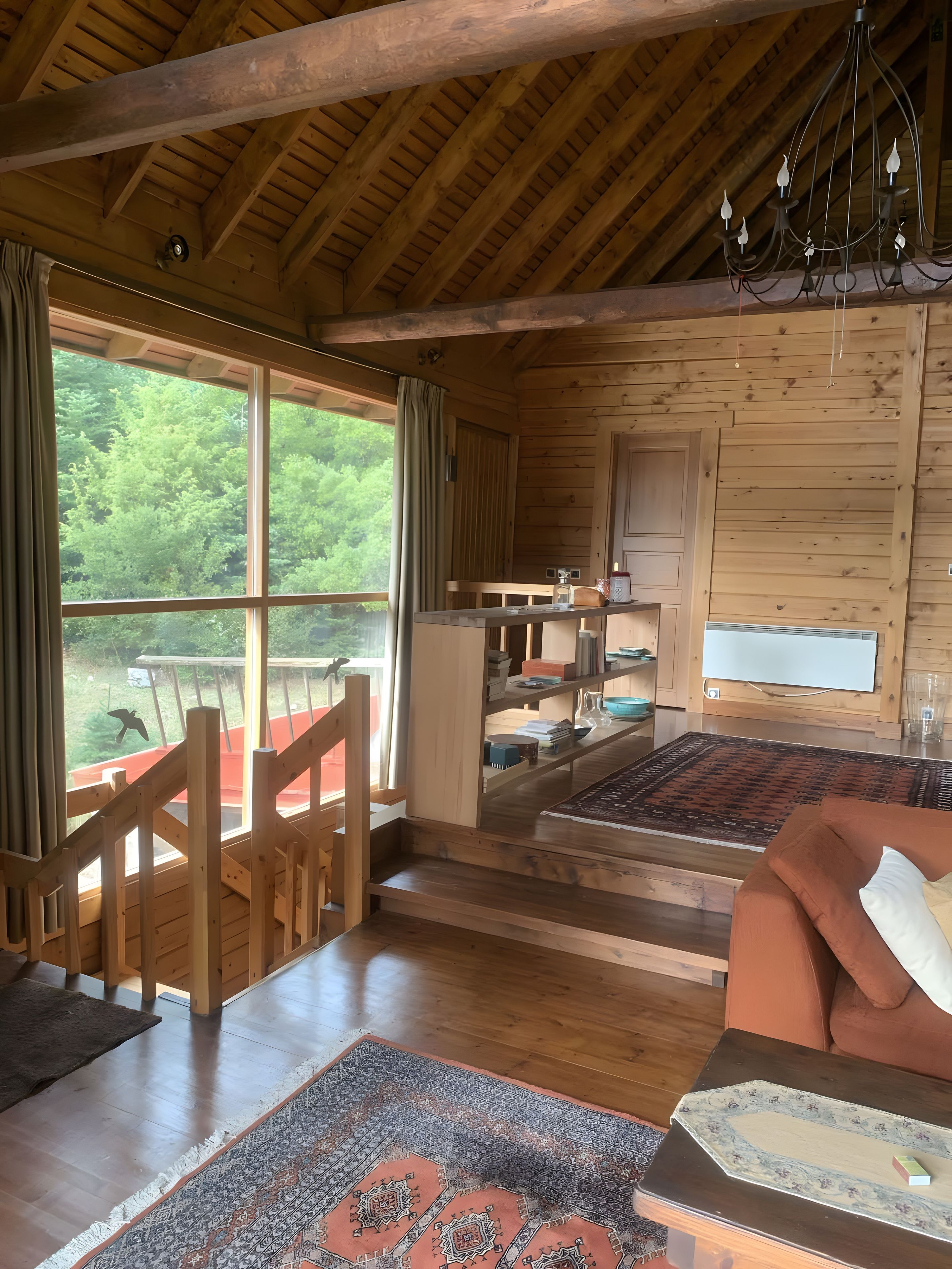 Ein Holzblock-Innenraum mit großem Fenster, einer Holztreppe und einer gemütlichen Sitzecke.