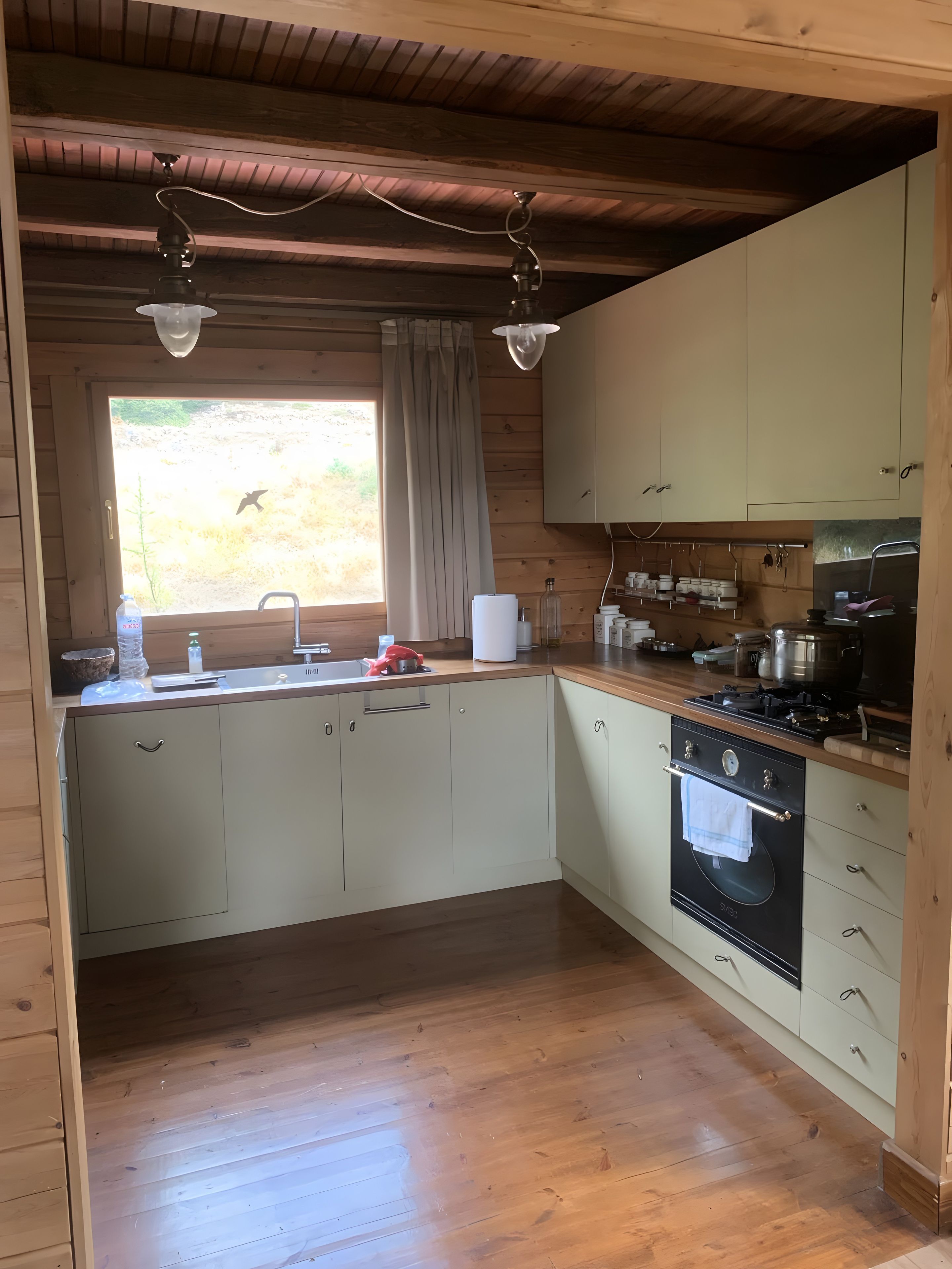 A compact kitchen with wooden cabinets, a built-in oven, and a window with curtains.