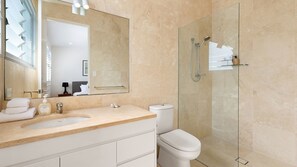 Un baño moderno con un espejo grande, un lavamanos, un inodoro y una ducha con mampara de vidrio.