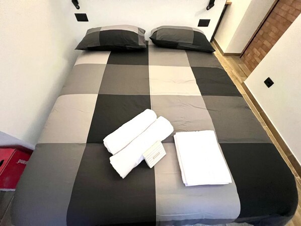 A bed with a checkered bedspread, two pillows, and neatly folded white towels. - New Listing (Sanremo)