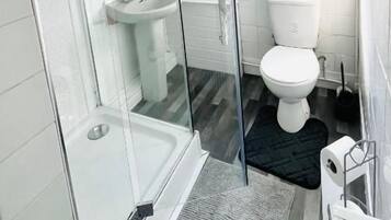 Un baño con cabina de ducha de vidrio, lavamanos blanco y retrete.