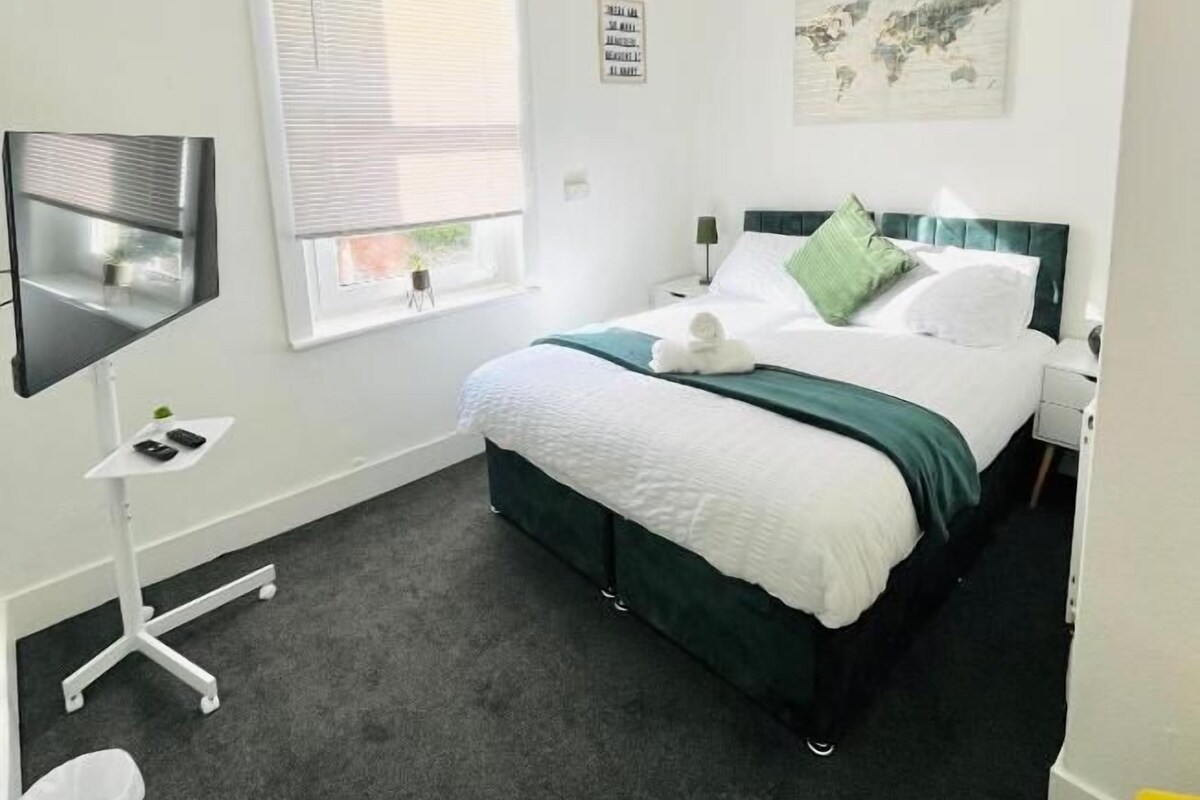 Een hotelkamer met een bed, een bureau, een stoel, een televisie en een raam met luxaflex.