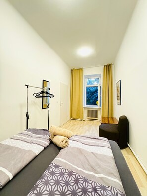 A small, well-lit room with two beds, a window with curtains, a radiator, and a chair. - Your Vienna Key Private Room for Two (Wien)