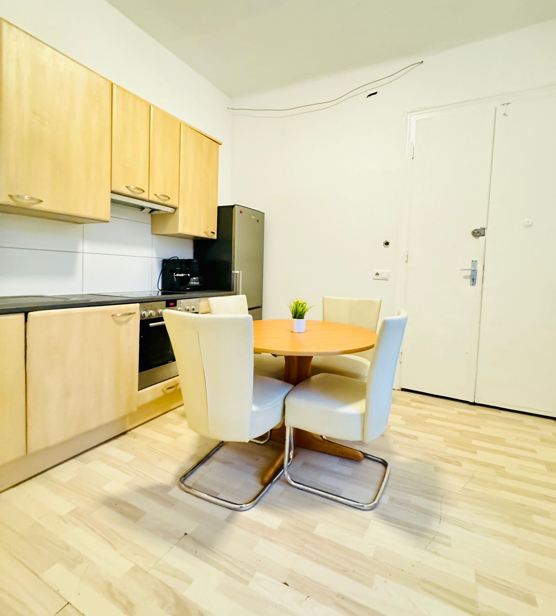Cocina compacta con armarios de madera, horno integrado, refrigerador y una mesa de comedor con cuatro sillas.
