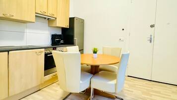 Cocina compacta con armarios de madera, horno integrado, refrigerador y una mesa de comedor con cuatro sillas.