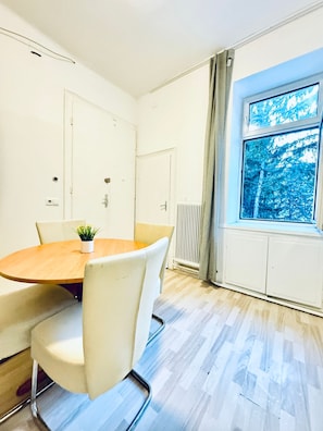 A conference room with a round table, white chairs, a potted plant, and a window with a view of trees. - Your Vienna Key Private Room for Two (Wien)