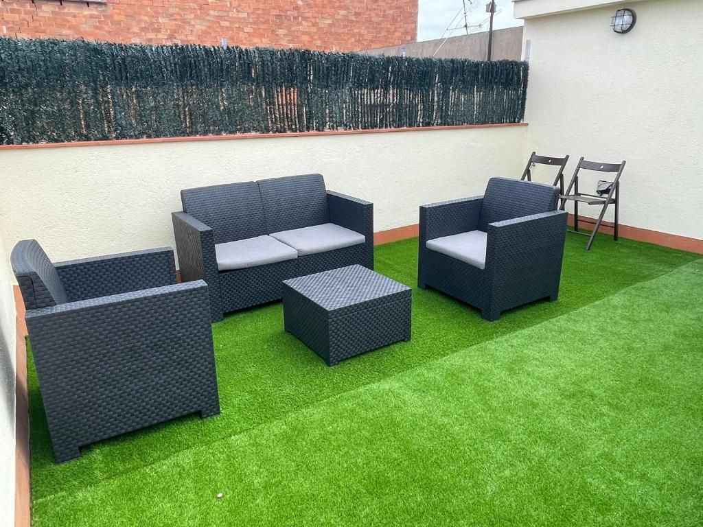 Mobiliario de mimbre para exteriores sobre césped artificial, pared de ladrillo y seto verde.