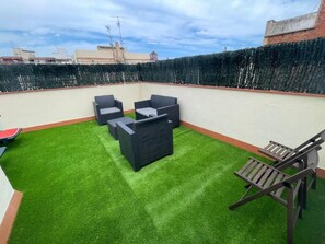 Una terraza en la azotea con césped artificial, mobiliario exterior y vistas a la ciudad.