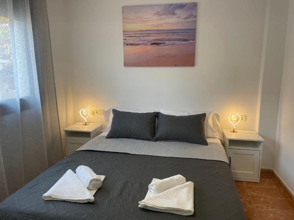 Habitación de hotel con cama, dos lámparas de noche, un cuadro de un atardecer y una ventana con cortinas.