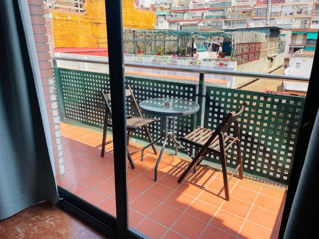Un balcón con una mesa y dos sillas, piso de baldosas y vista a un paisaje urbano con edificios y balcones.