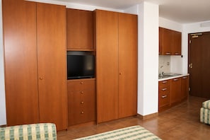 A room with wooden cabinets, a television, a kitchen area, and a patterned rug.
