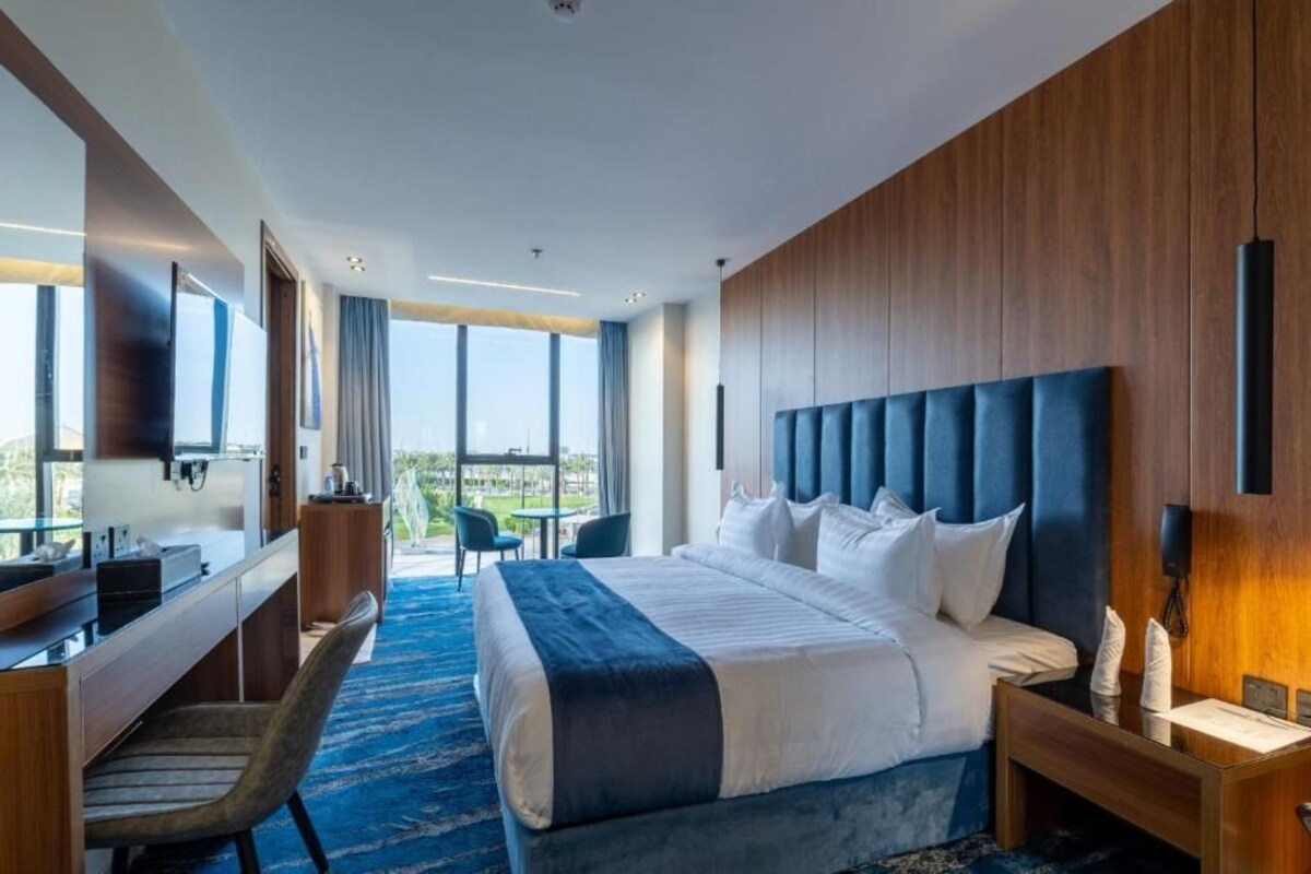 A hotel room with a large bed, a desk, a chair, and a view of the outdoors.