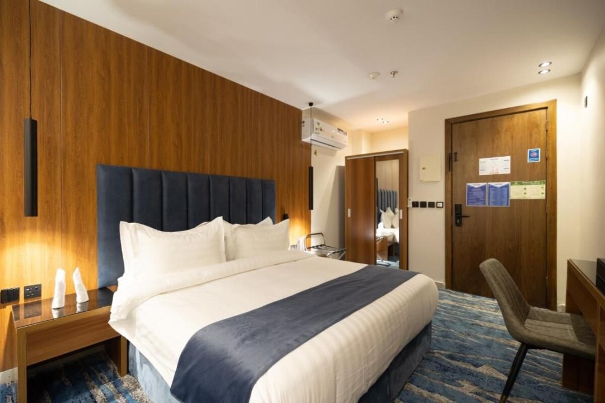 A hotel room with a large bed, a wooden headboard, a desk, and a chair.