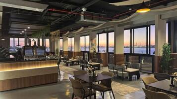 Un restaurant doté d’un bar, de nombreuses tables, de chaises et de grandes fenêtres offrant une vue sur le panorama urbain.