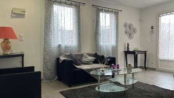 A living room with a sofa, a glass coffee table, a lamp, and a small table with decorative items.