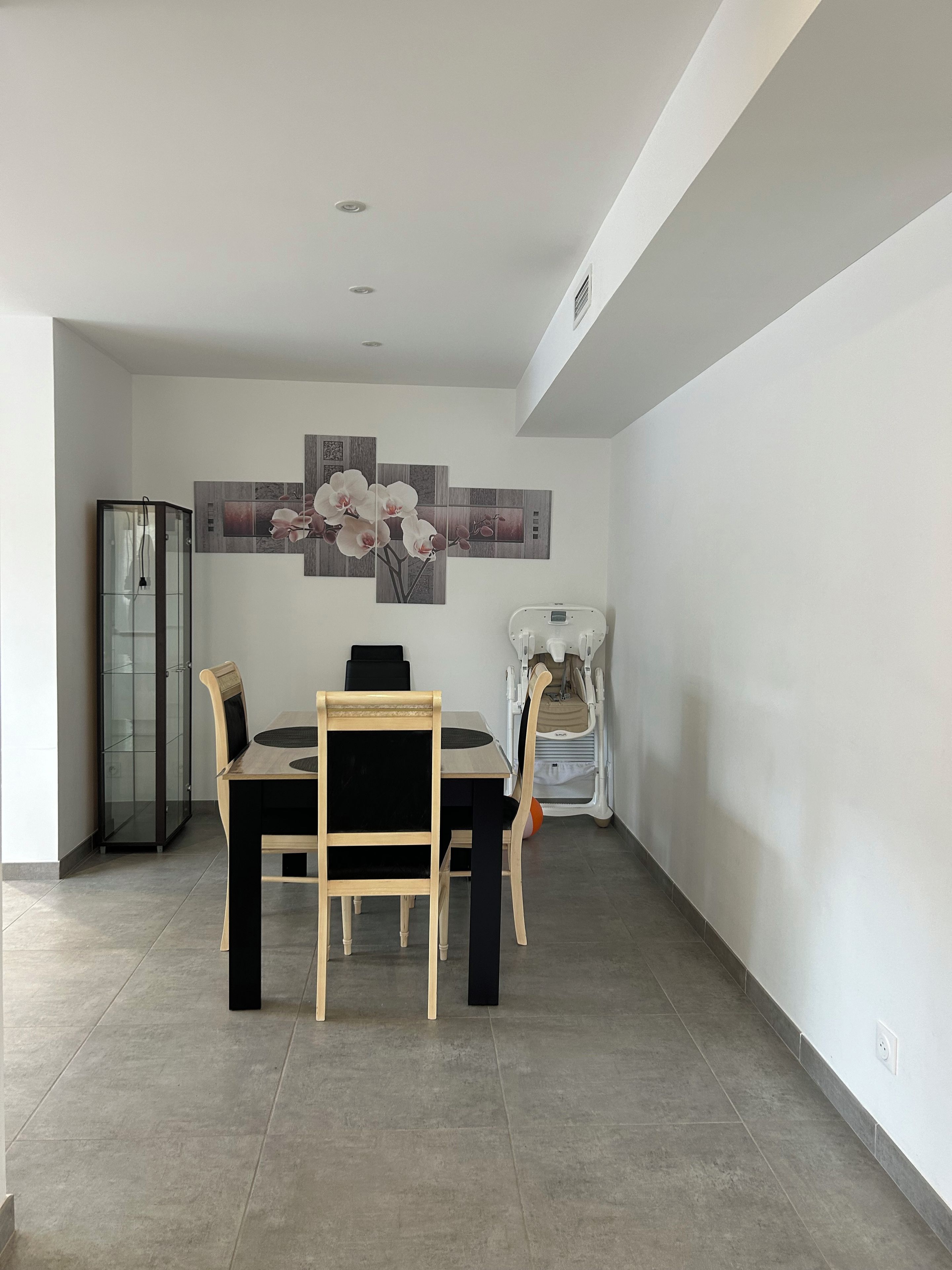 Un comedor con una mesa, sillas, un aparador de vidrio y una obra de arte colgada en la pared.