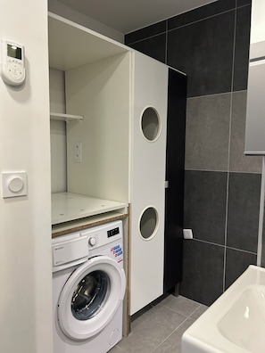 Une petite buanderie équipée d’un lave-linge, d’un étendoir et de toilettes.