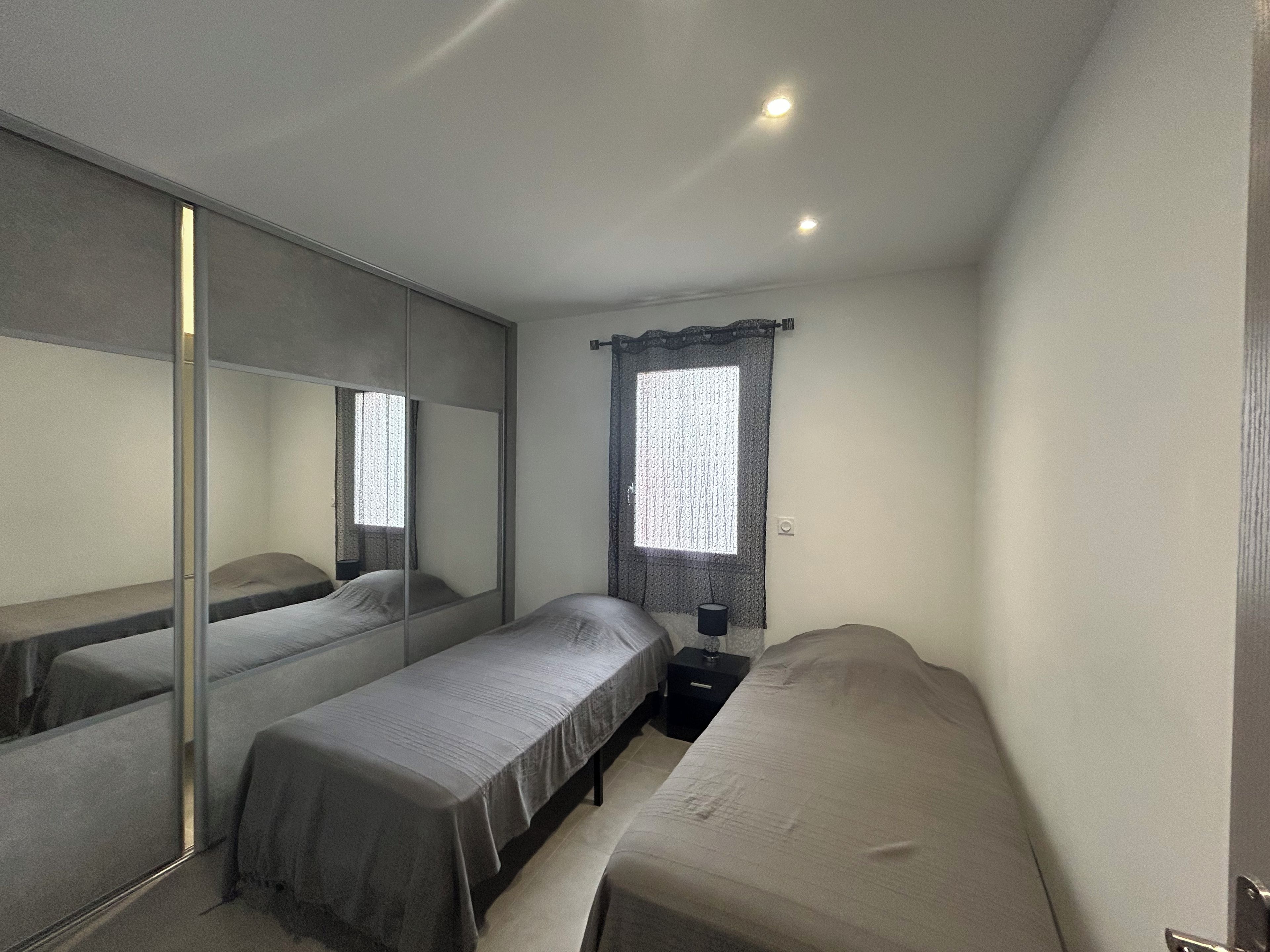 A bedroom with two single beds, a large mirror, a window with curtains, and a bedside table.