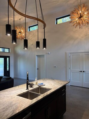 Une cuisine moderne dotée d’un îlot central, de luminaires suspendus et offrant une vue sur l’extérieur.