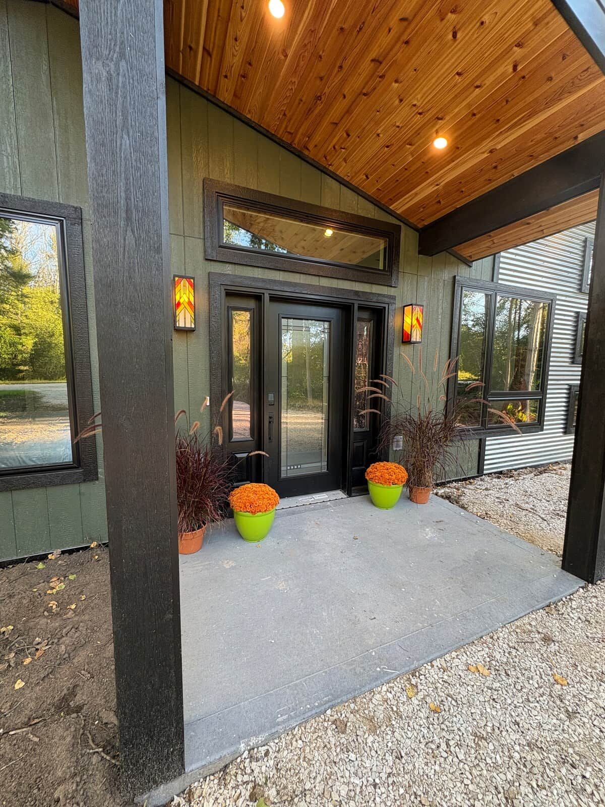 A modern house with a wooden ceiling, large windows, and a concrete porch with potted plants.