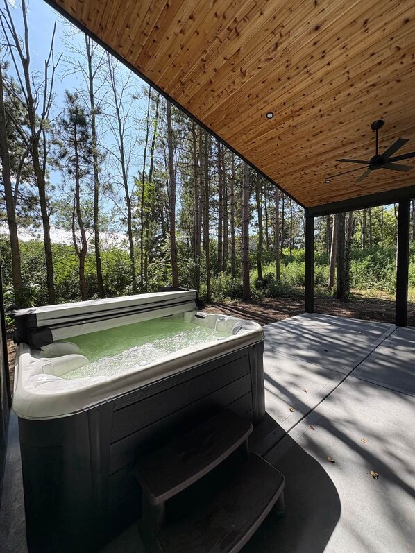 Un bain à remous installé dans une structure en bois à l’extérieur, avec vue sur une forêt.