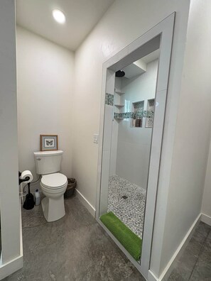Casa de banho com sanita, cabine de duche e um pequeno quadro emoldurado na parede.
