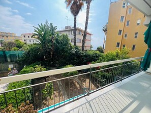 A balcony with a metal railing, a view of a residential area with buildings and greenery, and a clear sky. - New Listing (Sanremo)