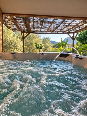 Ein Whirlpool unter einer hölzernen Pergola, umgeben von üppiger Vegetation und einer Bergkulisse.