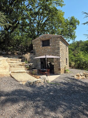 Ein Steinhaus mit Terrasse, Außenmöbeln und einer Treppe, die hinauf führt.